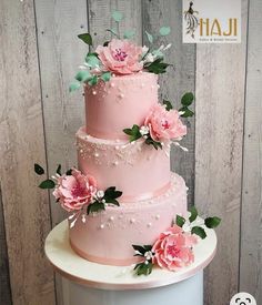 a three tiered cake with pink flowers on top and greenery around the edges