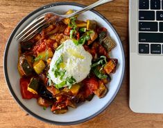 a plate of food next to a laptop on a wooden table with a silver fork