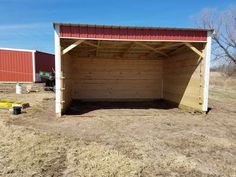 an empty garage in the middle of a field with two red and white buildings behind it