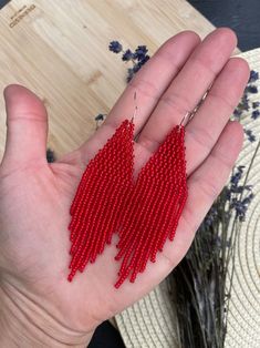 a person's hand holding two red beaded earrings