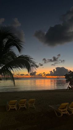 the sun is setting on the beach with lounge chairs