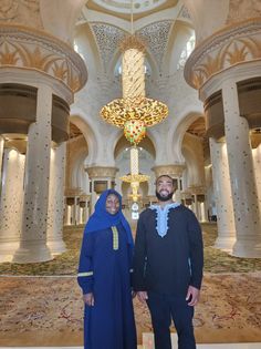 two people standing next to each other in a large room with columns and chandeliers