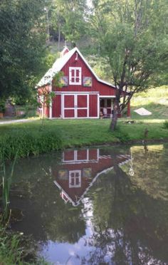 a small red house sitting on top of a lush green field next to a lake