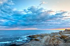 the sun is setting over the ocean and rocks