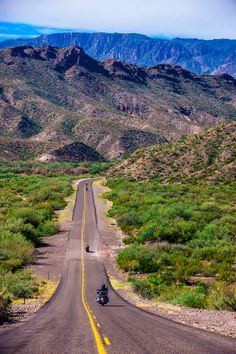 two motorcycles are driving down the road in front of mountains