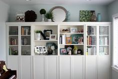 a white bookcase filled with lots of books next to a window and a piano