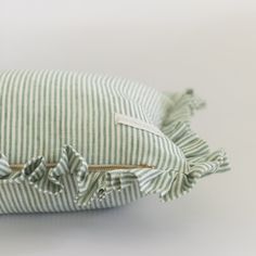 a green and white striped pillow with ruffles on the front, sitting on a white surface