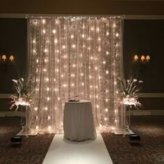 a white table topped with a vase filled with flowers next to a window covered in lights