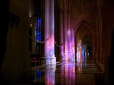 the light is shining on the floor and walls in this building, with columns that are lit by brightly colored lights