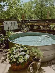 a large metal tub filled with water surrounded by potted plants and flowers next to a sign that says summer hot