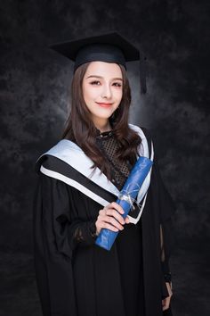 a woman wearing a graduation gown and holding a blue diploma in her hand, posing for the camera