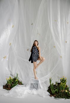 a woman standing on a rock in front of a white backdrop with plants and flowers