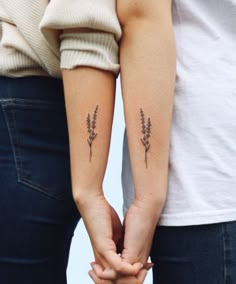 two people holding hands with small tattoos on their arms and the other hand behind them