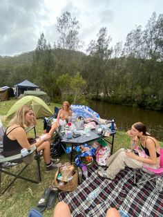 three women sitting at a picnic table on the grass next to a body of water