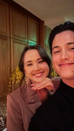 a man and woman posing for a photo in front of wooden cupboards with flowers