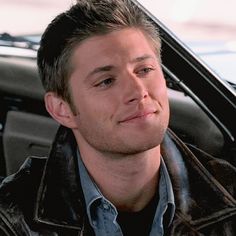 a man in a leather jacket is sitting in a car and looking at the camera