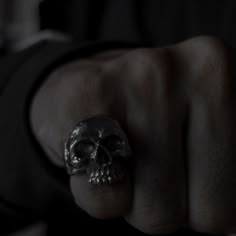 a person wearing a ring with a skull on it's middle finger in the dark