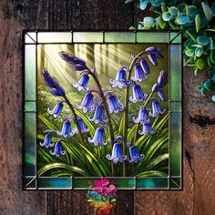 a stained glass window with blue flowers in it on a wooden table next to a potted plant