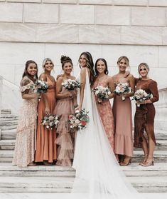 a group of women standing next to each other in front of a stone wall holding bouquets