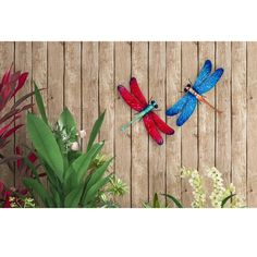 two dragonflies are sitting on the side of a wooden fence with flowers and plants around them