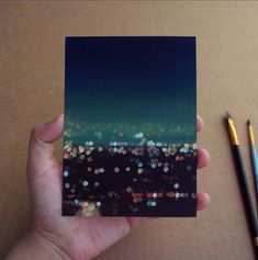 a person holding up a small card with glitters on it and a pen next to it