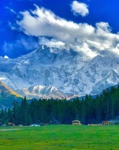 the mountains are covered with snow and clouds in the distance, as well as green grass