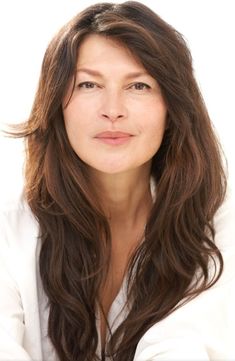 a woman with long brown hair and white shirt posing for the camera in front of a white background