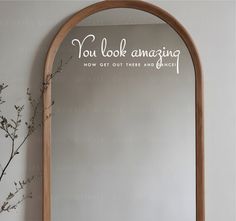 an arched mirror with the words you look amazing written on it and a plant next to it