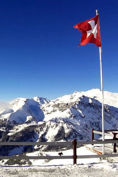 a red and white flag on top of a snow covered mountain with mountains in the background