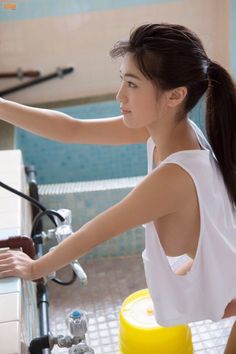 a young woman is washing dishes in the kitchen with her hand on the sink faucet