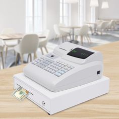 an electronic cash register sitting on top of a wooden table with chairs in the background