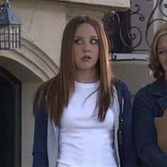 two women standing next to each other in front of a building with an iron gate