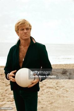 a man on the beach holding a ball in one hand and looking at the camera