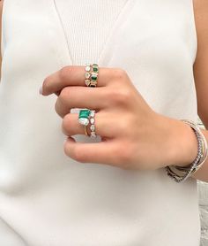 a close up of a person's hand with two rings on their fingers and an emerald ring