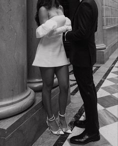 a man and woman standing next to each other in front of columns wearing high heels