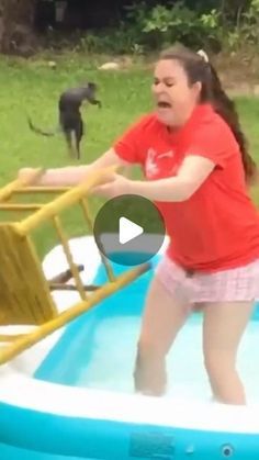 a woman in a red shirt is playing with a black dog on a trampoline