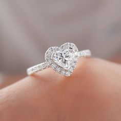 a woman's hand with a heart shaped diamond ring on top of her finger