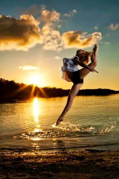 a woman jumping into the air on top of a body of water in front of a sunset