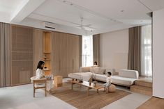 two people are sitting in the middle of a living room with white furniture and wood paneling