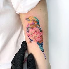 a colorful bird with flowers on its arm and leg is shown in this tattoo artist's photo