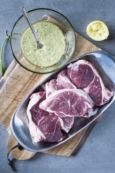 raw meat on a cutting board next to a bowl of dressing