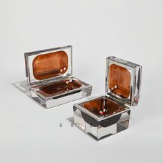 two square shaped glass dishes sitting next to each other on a white surface with one being filled with liquid