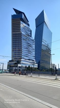 two very tall buildings sitting next to each other on the side of a road in front of a blue sky