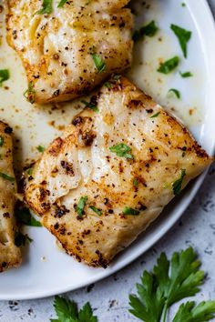 three pieces of chicken on a white plate with parsley sprinkled around it