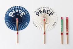 three paper fans and two chopsticks on a white surface with words written on them