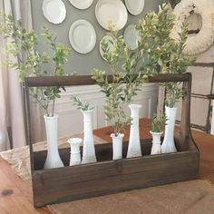 a wooden tray with vases and greenery in front of plates on the wall