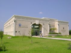 two people walking in front of a large building with trees and grass on the lawn