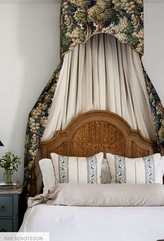 a bed with a canopy over it and pillows on the headboard, in front of a window