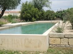 an empty swimming pool in the middle of a field with trees and bushes around it