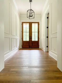 an empty hallway with wooden floors and two doors leading to the front door that leads to another room